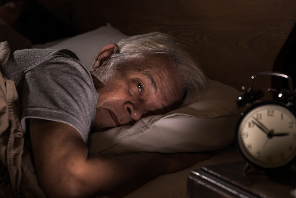 older adult lying awake in bed at night looking at clock experiencing insomnia