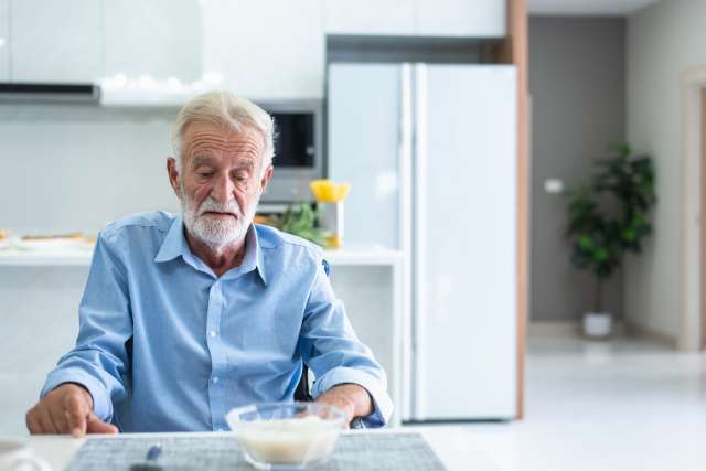 A person over 50 is not feeling hungry while sitting at the table