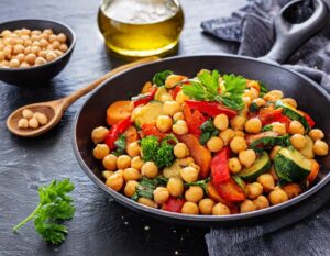 A healthy bowl of chickpeas with olive oil, herbs, and vegetables on a kitchen table with an older adult 