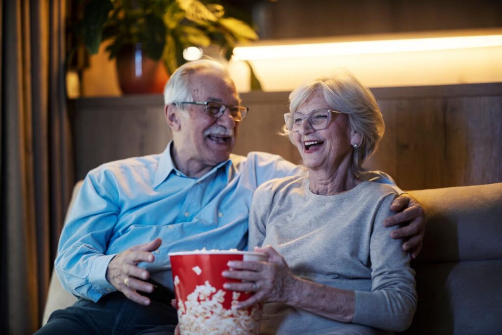 An older couple comfortably watching television at home in the evening.