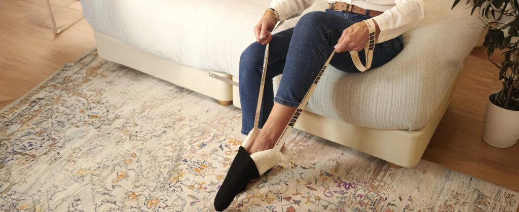 Senior using a sock aid device to put on socks without bending over.